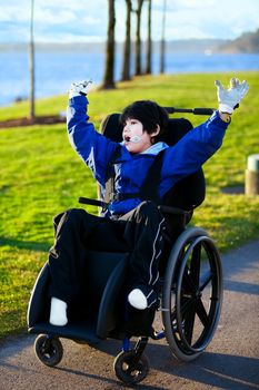 Disabled boy in wheelchair enjoying day at park, arms raised in happiness