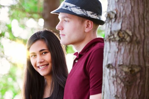 Young interracial couple standing among trees, sunlight streaming