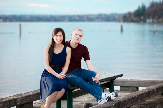 Happy young interracial couple sitting together on dock over lake