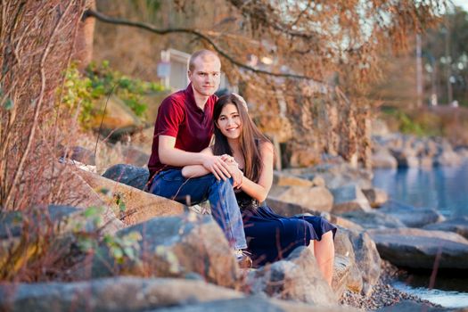 Young interracial couple rekaxing together on rocky shoreline by lake