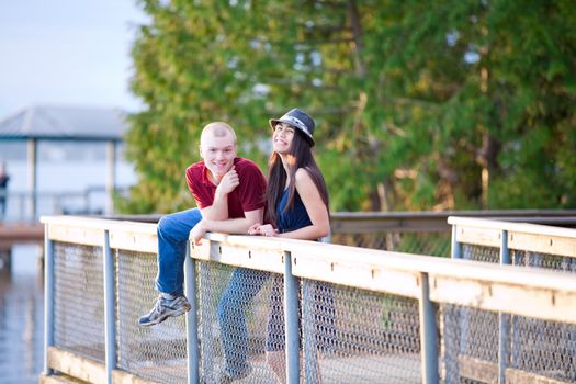 Young happy interracial couple standing together on wooden pier overlooking lake, laughing