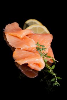 Smoked salmon with fresh herbs and lemon isolated on black background. Culinary seafood.