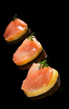 Luxurious seafood canape. Smoked salmon on lemon slices isolated on black background.