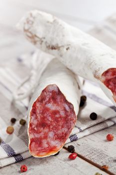 Luxurious traditional fuet sausage on kitchen towel on white wooden textured background with colorful peppercorns. Traditional mediterranean eating.