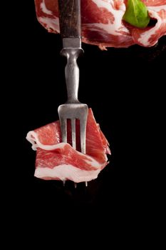 Luxurious delicious traditional italian parma ham on old fork and in background with fresh salad. Culinary cooking.
