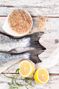 Delicious mediterranean seafood concept. Two fresh fish tail, lemon and fresh herbs on white textured wooden background. Culinary seafood concept in marine white.