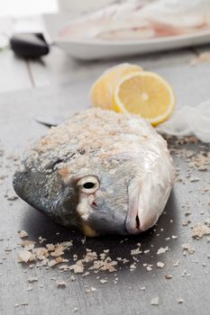 Fresh sea bream with sea salt crystals and lemon on kitchen table. Preparing seafood concept.