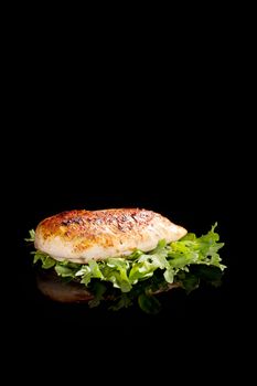 Delicious juicy chicken steak with fresh lettuce isolated on black background with reflection. Culinary luxurious eating.