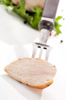 Delicious juicy chicken piece on fork, fillet with salad in background. Culinary chicken meat concept.