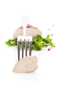 Juicy delicious chicken piece on silver fork, chicken steak with pepper corns in background isolated on white background. Culinary eating concept. 