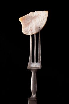 Delicious juicy chicken piece on old fork isolated on black background. Culinary meat eating concept.