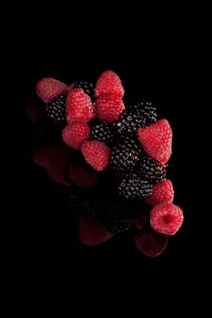 Delicious ripe raspberries and blackberries isolated on black background. Luxurious healthy berries, fresh tasty summer fruits.