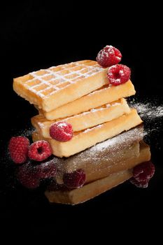 Waffles with delicious ripe raspberries isolated on black background. Culinary traditional sweet dessert.