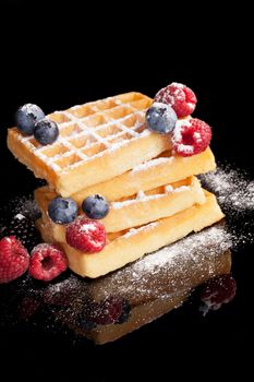 Delicious waffles with blueberries, raspberries and blackberries isolated on black background. Luxurious dessert background.