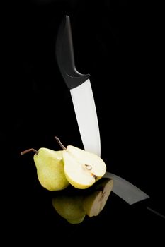 Pear piece and black and white ceramic knife isolated on black background. Luxurious healthy summer fruit.