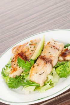 Culinary seafood eating. Grilled fish fillet with fresh rocket and lettuce salad on plate isolated on brown background. 