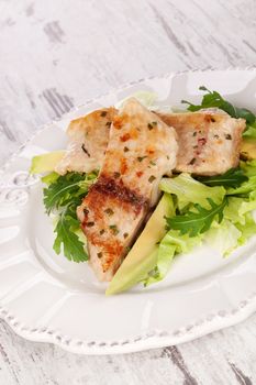 Grilled fish fillet with fresh vegetable and salad on white plate on white wooden textured background. Luxurious fish eating, healthy cuisine, superfood.