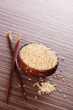 Luxurious minimal natural brown rice background. Raw rice crop in brown round asian bowl on brown background with chopsticks. 