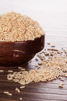 Brown rice in brown wooden round oriental bowl on brown background. Asian rice eating concept.