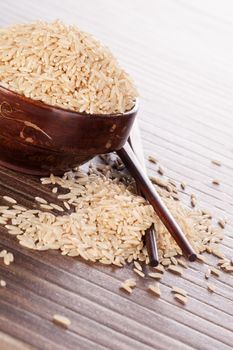 Brown rice background. Rice in wooden round bowl with chopsticks on brown background. Culinary natural rice eating.