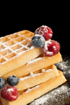 Traditional culinary sweet food. Sugared waffles with berries isolated on black background.