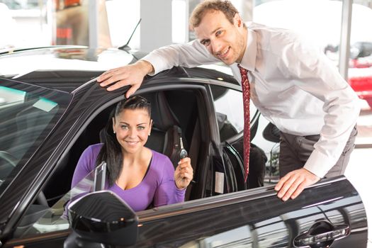 Salesman in car dealership presenting a car to female customer