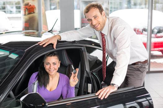 Salesman in car dealership presenting a car to female customer