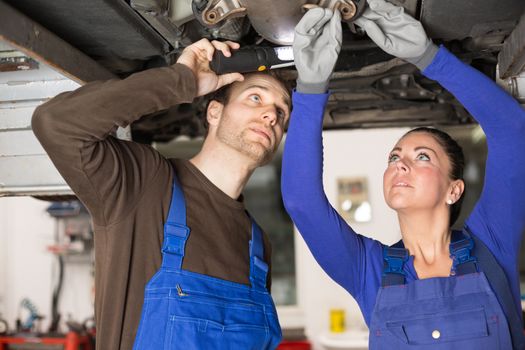 Two mechanics repairing or inspecting a car on hydraulic lift