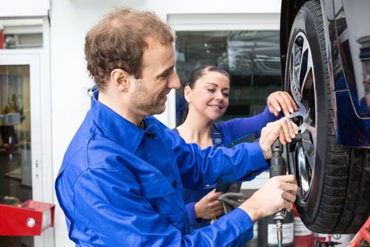 Two mechanics changing a wheel on a car standing on a hydraulic ramp