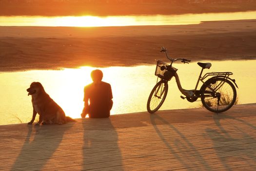 Silhouetted man with a dog watching sunset at Mekong river waterfront, Vientiane, Laos, Southeast Asia