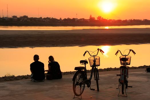 Silhouetted couple watching sunset at Mekong river waterfront, Vientiane, Laos, Southeast Asia