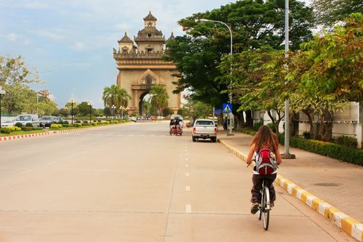Young woman riding bike near Victory Gate Patuxai, Vientiane, Laos, Southeast Asia