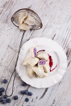 Appetizing european sweet dessert. Sweet dumpling with jam and fresh blueberries on white wooden background. 
