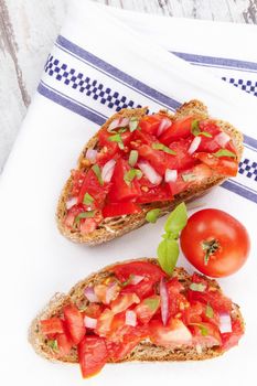 Culinary bruschetta eating, rustic style. Bruschetta bread with fresh tomatoes on white cloth, top view. Delicious mediterranean eating. 