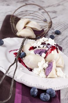 Culinary sweet dessert eating. Blueberry filled dumpling with jam and fresh fruit on plate on white wooden background. Rustic, country style eating.