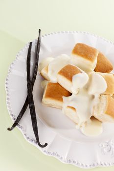 Dumplings with vanilla sauce and vanilla sticks on white plate isolated on yellow background. Culinary sweet eating. 