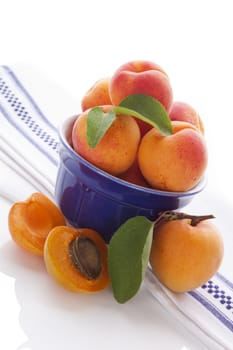 Fresh apricots on white and blue table cloth on white background. Healthy summer fruit eating. 