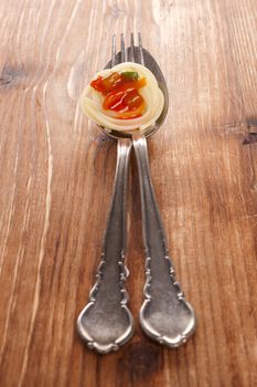 Traditional pasta eating. Pasta with red sauce on silver spoon with fork isolated on brown wooden background.