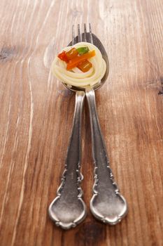 Culinary pasta eating. Pasta with colorful vegetable on silver spoon with fork isolated on brown wooden background.