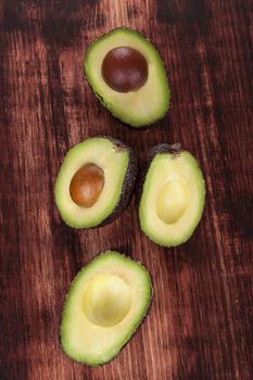 Ripe avocado fruit also known as alligator pear halves, few with core, few without on brown wooden background, top view. Healthy vegetarian eating.