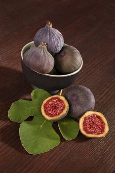 Fresh figs with leaf in bowl on dark brown wooden background. Healthy fresh fruits.
