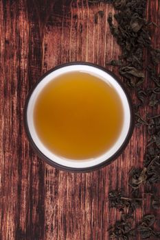 Traditional tea drinking. Dry tea crop, green tea in cup on brown wooden background, top view. 