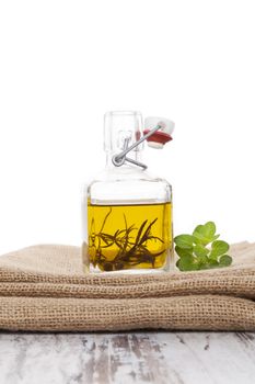 Extra virgin olive oil in glass bottle with fresh herbs on burlap cloth on white wooden background. Culinary cooking and eating. 