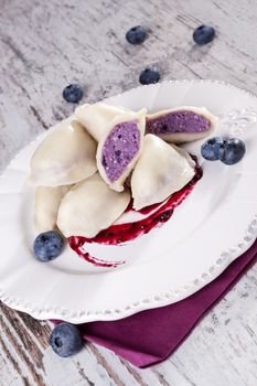 Blueberry dumplings with jam on white vintage plate on white wooden background. Culinary sweet food eating. 