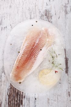 Raw frozen fish fillet with fresh herbs and lemon on white wooden textured background. Culinary seafood eating. 