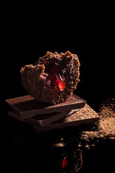 Delicious chocolate muffin with cocoa powder on chocolate bar isolated on black background. Culinary sweet dessert.