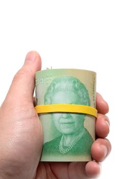 Hand holding a roll of 20 dollars Canadian with yellow plastic band over the eyes of the queen Elizabeth.