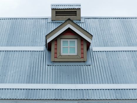 Architectural detail of small dormer window in metal sheet roof of residential house