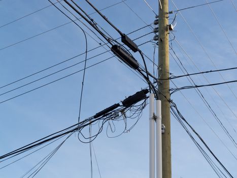 Wooden pole hung with confusing and messed-up electricity power cables and telephone lines for residential utilities supply