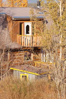 View through trees wild garden vegetation of hidden balcony and white painted door of older timber frame house